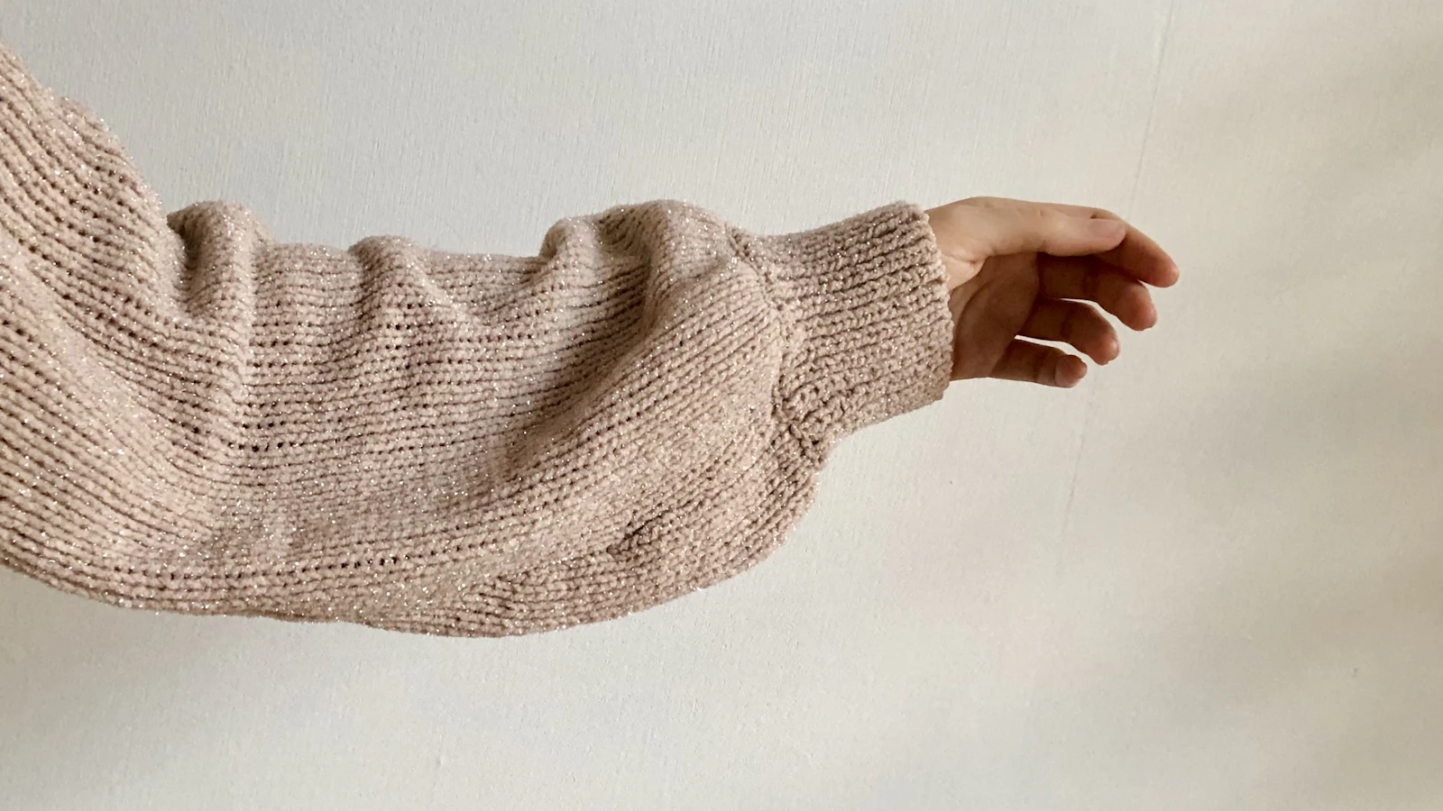 Arm mit beigem Strickpullover-Ärmel und sichtbarem Rippbündchen.