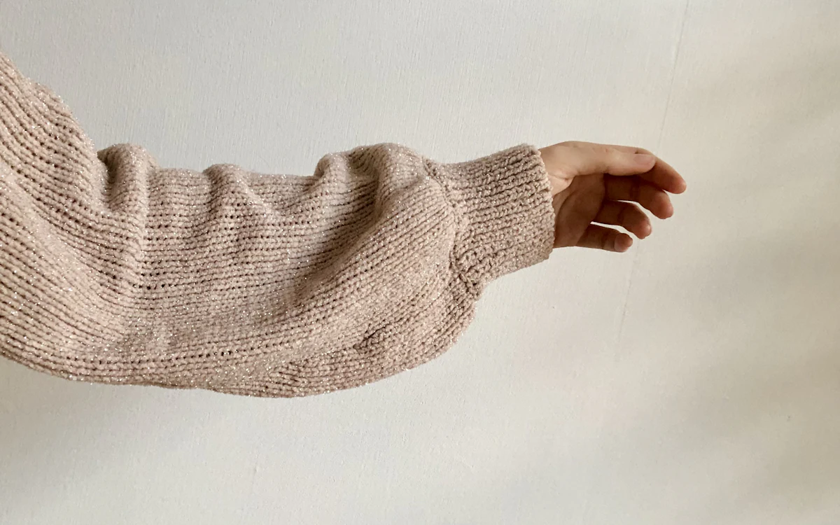 Arm mit beigem Strickpullover-Ärmel und sichtbarem Rippbündchen.