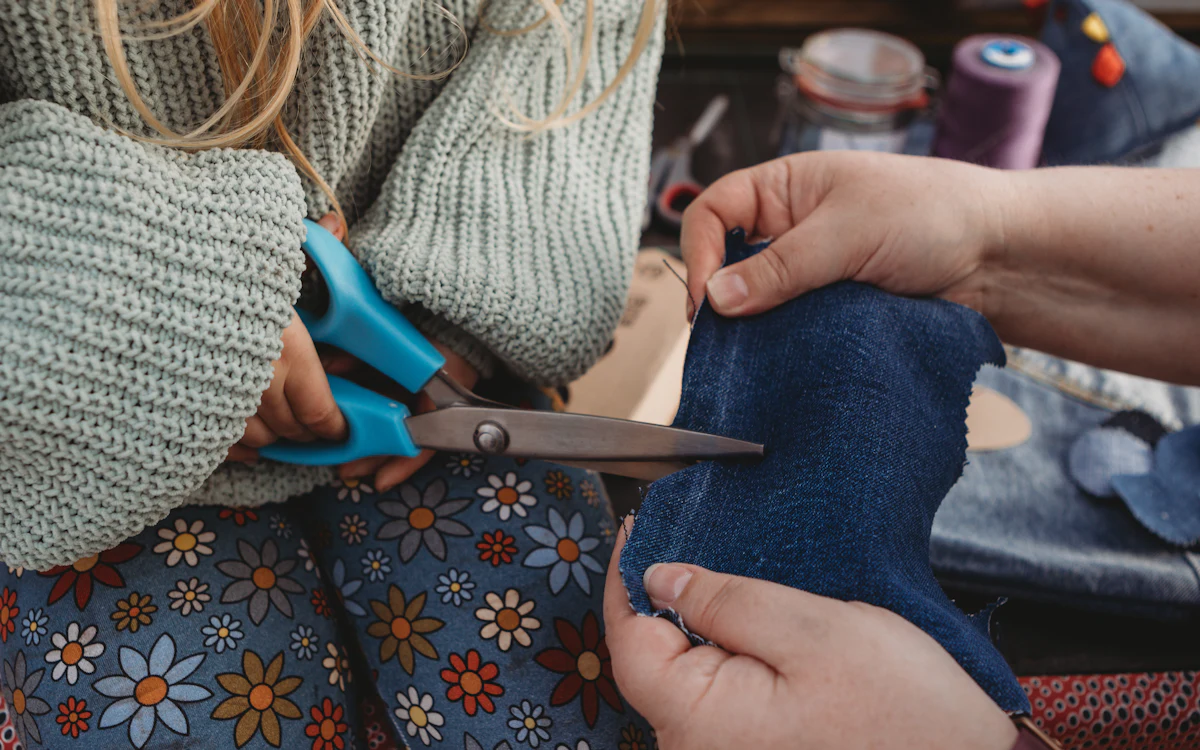 Kinderhände mit Schere über blauem Stoff neben Nähutensilien.