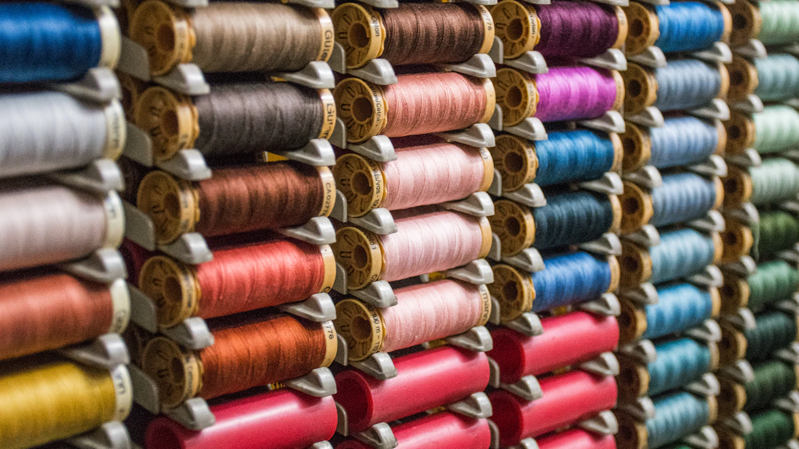 Viele bunte Garnrollen dicht nebeneinander in einem Regal.