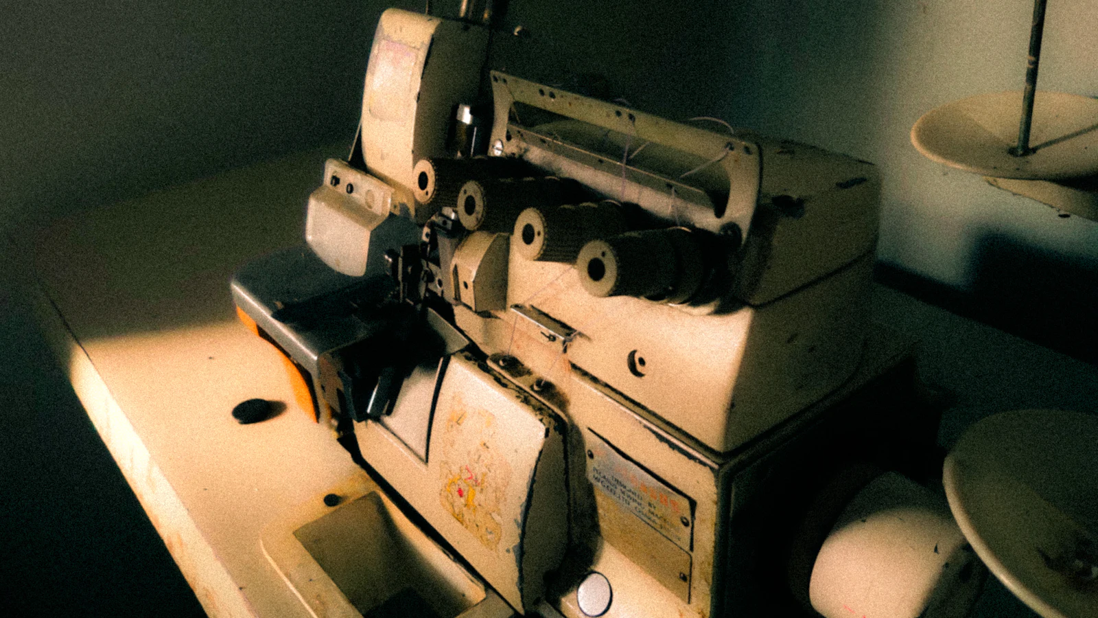 Alte Overlockmaschine mit mehreren Garnrollen im Werkstattlicht.