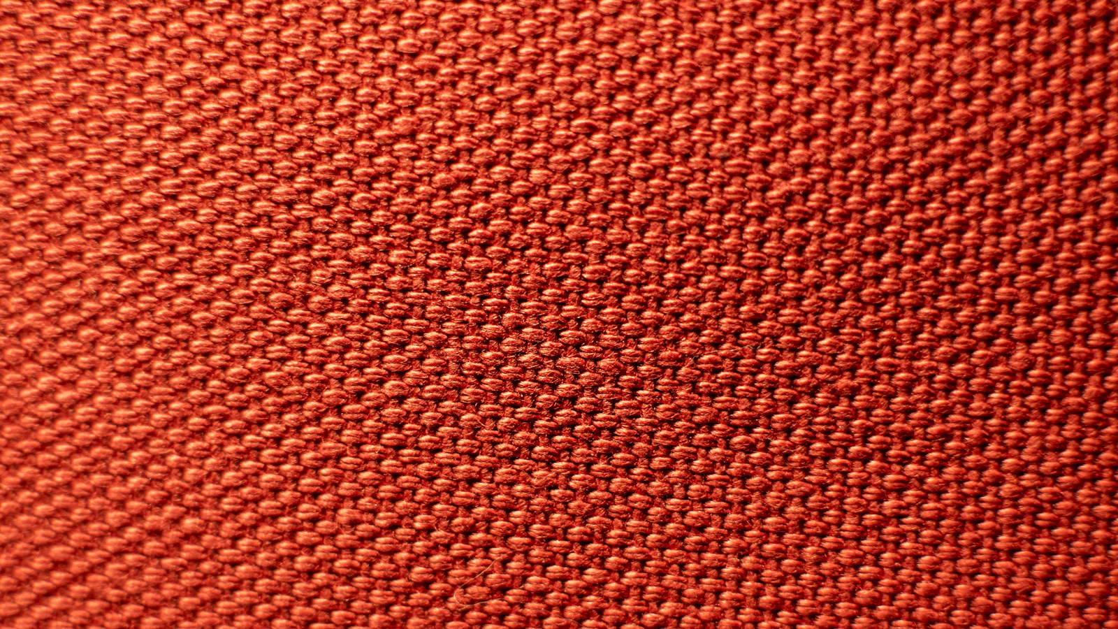 Rot-orangefarbene Maschenware in Nahaufnahme mit sichtbarer Maschenstruktur.
