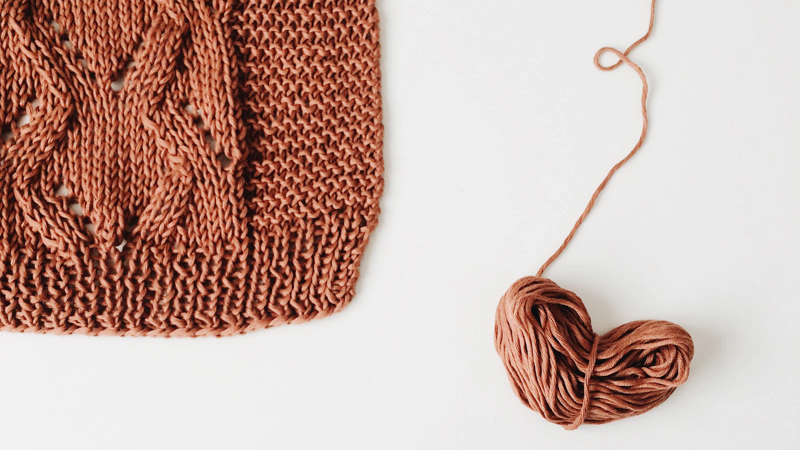 Rosé gefärbter Wollstoff mit Strickstruktur neben einem Wollknäuel.